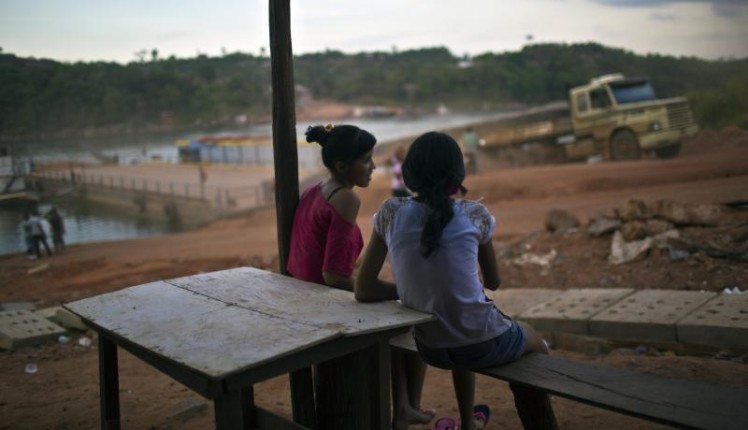Girls look on as a logging truck disembarks from a ferry in the Amazonian state of Para, Brazil. Photo via Getty Images.